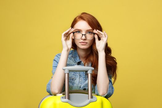 Travel and Lifestyle Concept: Portrait of a shocked girl in denim dress with suitcase looking at camera isolated over golden yellow background