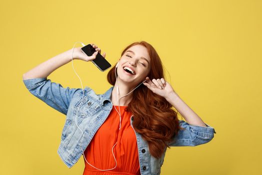 Lifestyle and Music Concept: Beautiful young curly red hair woman in headphones listening to music and dancing on vivid yellow background