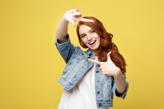 Portrait of young beautiful ginger woman with freckles cheerfuly smiling making a camera frame with fingers. Isolated on yellow background. Copy space.
