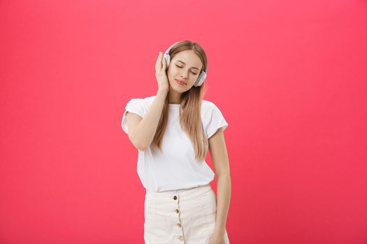 Funny woman with headphones dancing singing and listening to the music from a smart phone isolated on a pink background.