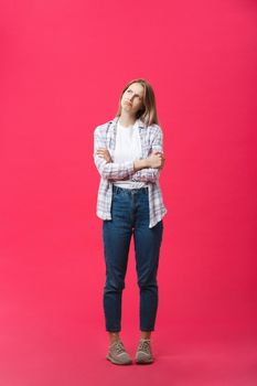Thoughtful frowning young woman standing and thinking over pink background