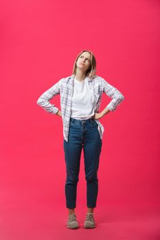 Thoughtful frowning young woman standing and thinking over pink background