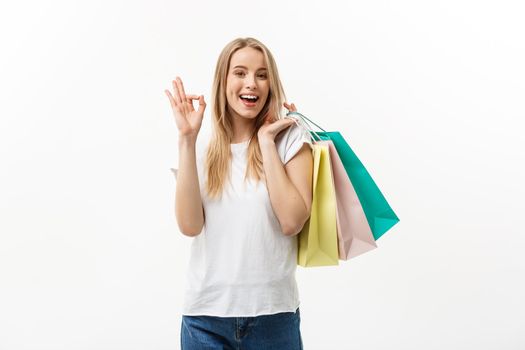 Smiling attractive woman holding shopping bags doing ok sign on white background with copyspace