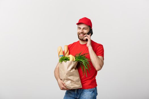Handsome grocery delivery man talking to mobile and holding grocery paper bag.