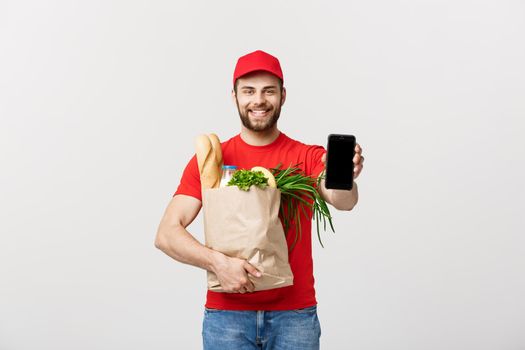 Delivery Concept: Handsome Caucasian grocery delivery courier man in red uniform with grocery box with fresh fruit and vegetable