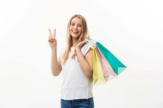 Smiling attractive woman holding shopping bags doing peace sign on white background with copyspace