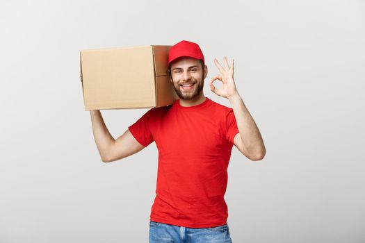 Cheerful young delivery man in red cap standing with parcel post box isolated over white background showing okay sign gesture.