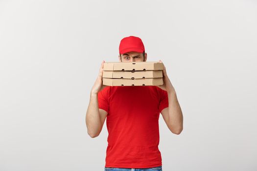 A Deliveryman hidden behind a large stack of pizza boxes he is carrying. Isolated over grey background.