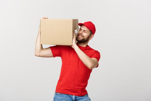 Deliver Concept: Young caucasian handsome delivery man holding a box on shoulder. Isolated over grey background.