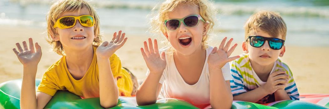 Children sit on an inflatable mattress in sunglasses against the sea and have fun BANNER, LONG FORMAT
