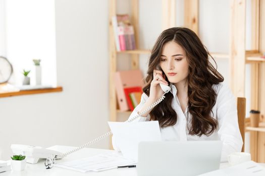 Tired beautiful Businesswoman holding hand on head while working on computer and some business documents in bright office