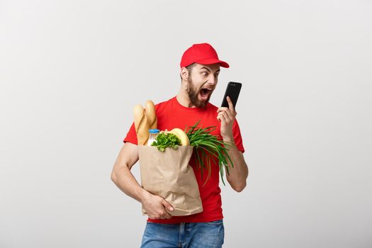 Delivery Concept: Handsome Caucasian grocery delivery courier man in red uniform with grocery box with fresh fruit and vegetable