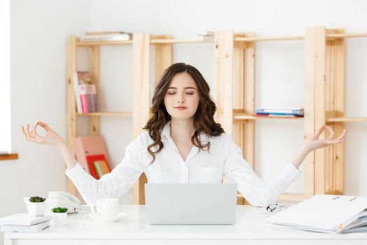 Business and Health Concept: Portrait young woman near the laptop, practicing meditation at the office desk, in front of laptop, online yoga classes, taking a break time for a minute.