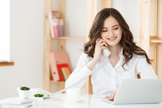 Young businesswoman or secretary sitting at desk and working. Smiling and looking at camera