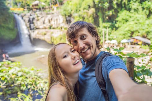smiling couple, man and woman making selfie on a waterfall background