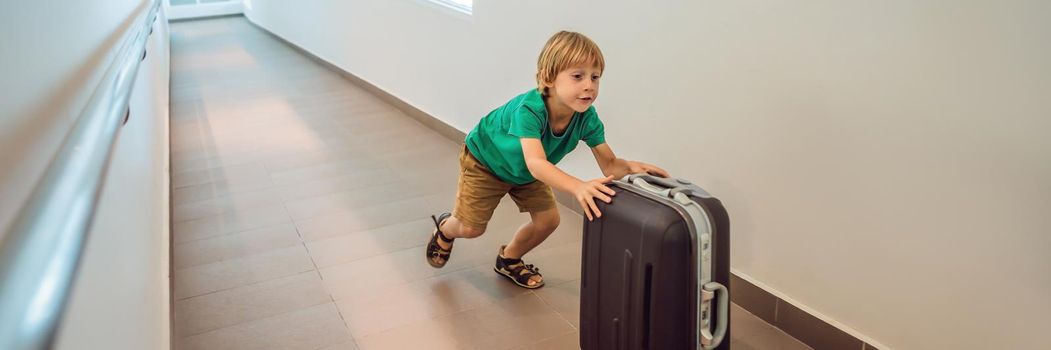 Funny little boy going on vacations trip with suitcase at airport, indoors BANNER, LONG FORMAT