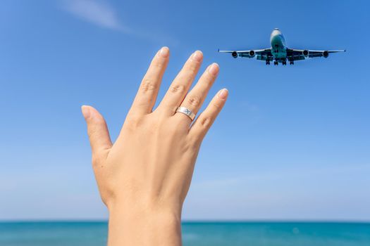 Female hand with a ring with a drawn plane holding a plane flying in the sky. Traveling on an airplane concept. Text space. Impressive paradise. Hot beach Mai Khao. Amazing landscape