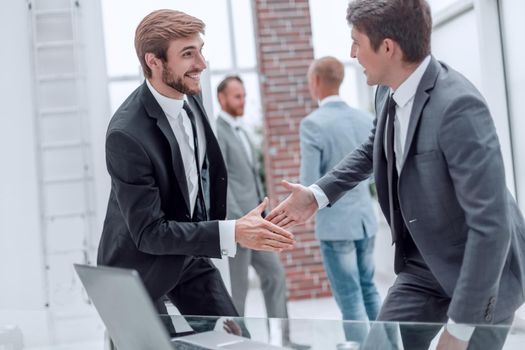 happy business people shaking hands near the desktop