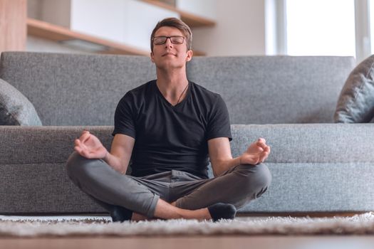 casual guy sitting in Lotus position on carpet in his living room