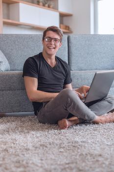 young man working on laptop sitting on carpet in living room