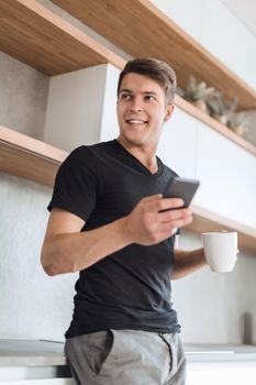 handsome guy with a Cup of coffee and a smartphone standing in the kitchen