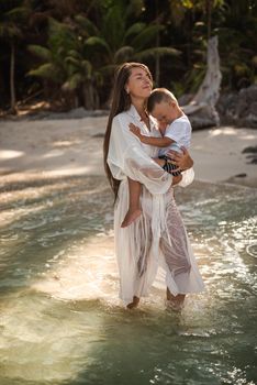 mother is walking along the azure sea and carries son in her arms