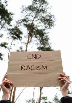 Female hands holding cardboard with text END RACISM outdoors. Nature background. Protester activist