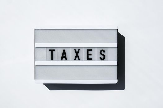 Lightbox board on a white background with the words TAXES in black letters.