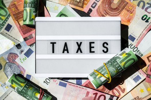 Lightbox board with word TAXES in black letters around Euro banknotes. Tax payment and filing concept. Money, Business, finance, investment, saving and corruption
