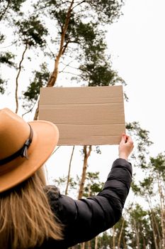 Female hands standing with cardboard outdoors. Nature background. Copy space for text. Protester activist