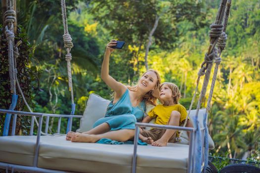 Mother and son swinging in the jungle rainforest of Bali island, Indonesia. Swing in the tropics. Swings - trend of Bali. Traveling with kids concept. What to do with children. Child friendly place