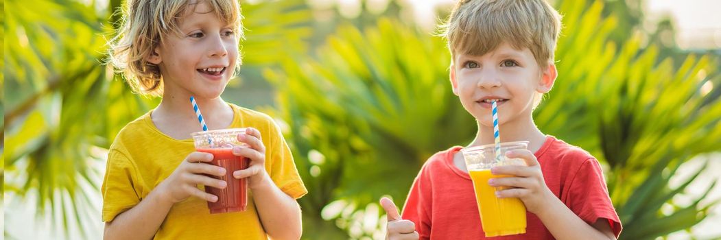 BANNER, LONG FORMAT Two boys drink healthy smoothies against the backdrop of palm trees. Mango and watermelon smoothies. Healthy nutrition and vitamins for children