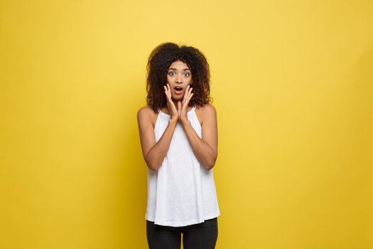 Smiling beautiful young African American woman in white T-shirt posing with hands on chin. Studio shot on Yellow background. Copy Space.