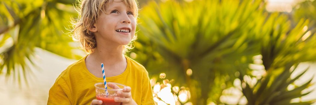 Boy drink healthy smoothies against the backdrop of palm trees. Watermelon smoothies. Healthy nutrition and vitamins for children BANNER, LONG FORMAT