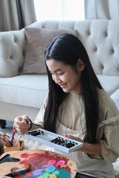 Cheerful asian girl hand choosing acrylic paint tube for her artwork.