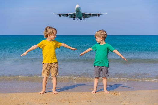 Two happy boys have fun on the beach watching the landing planes. Traveling on an airplane with kids concept. Text space. Island Phuket in Thailand. Impressive paradise. Hot beach Mai Khao. Amazing landscape