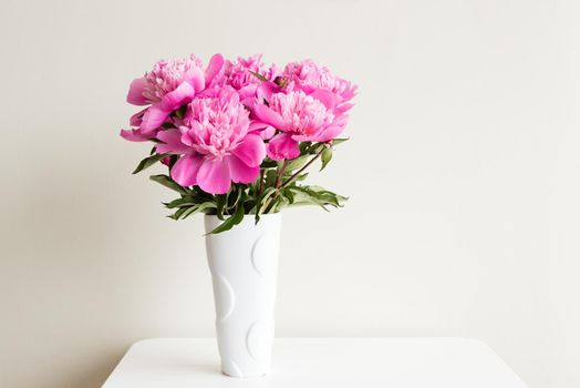 Pink peonies in white vase on table against neutral background