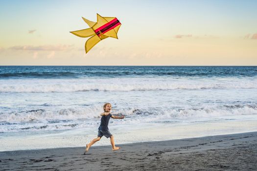 Happy young boy flying kite on the beach at sunset