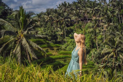 Beautiful young woman walk at typical Asian hillside with rice farming, mountain shape green cascade rice field terraces paddies. Ubud, Bali, Indonesia. Bali travel concept