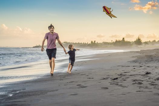 Young father and his son running with kite on the beach.
