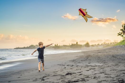 Happy young boy flying kite on the beach at sunset