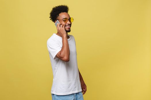 Portrait of cool young black guy talking on cellphone. Isolated on yellow background