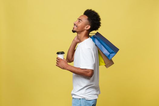 Handsome African American with shopping bag and take away coffee cup. Isolated over yellow gold background.
