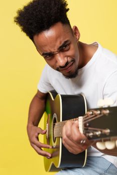 Young handsome African American retro styled guitarist playing acoustic guitar isolated on yellow gold background.