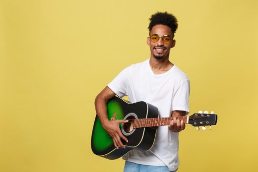 Happy african american musician man posing with a guitar, over golden yellow background.