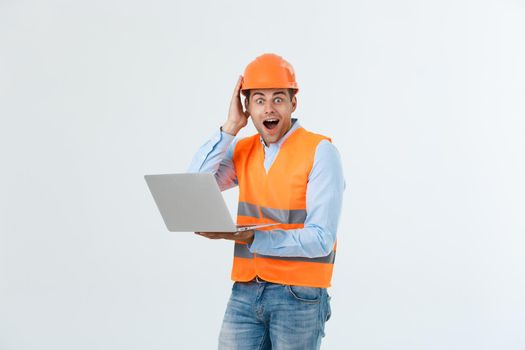 Portrait of a surprised engineer holding his laptop over gray background.