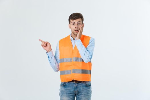 Handsome young professional engineer man over grey wall wearing orange vest amazed and surprised pointing with fingers.