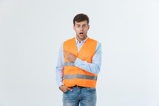 Handsome young professional engineer man over grey wall wearing orange vest amazed and surprised pointing with fingers.