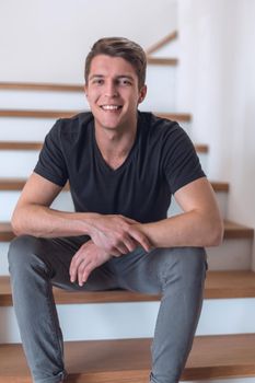 cheerful young man sitting on the steps in his house