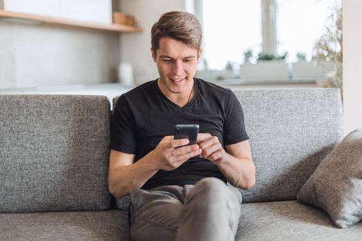 smiling young man reading correspondence on his smartphone